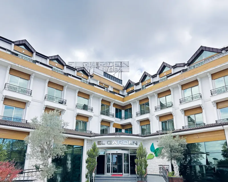 The El Garden hotel building: entrance with the EL GARDEN sign, balconied façade and olive trees