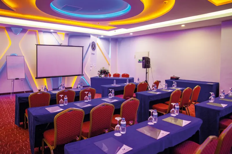 Meeting hall set up classroom-style: projection screen, tables and red chairs